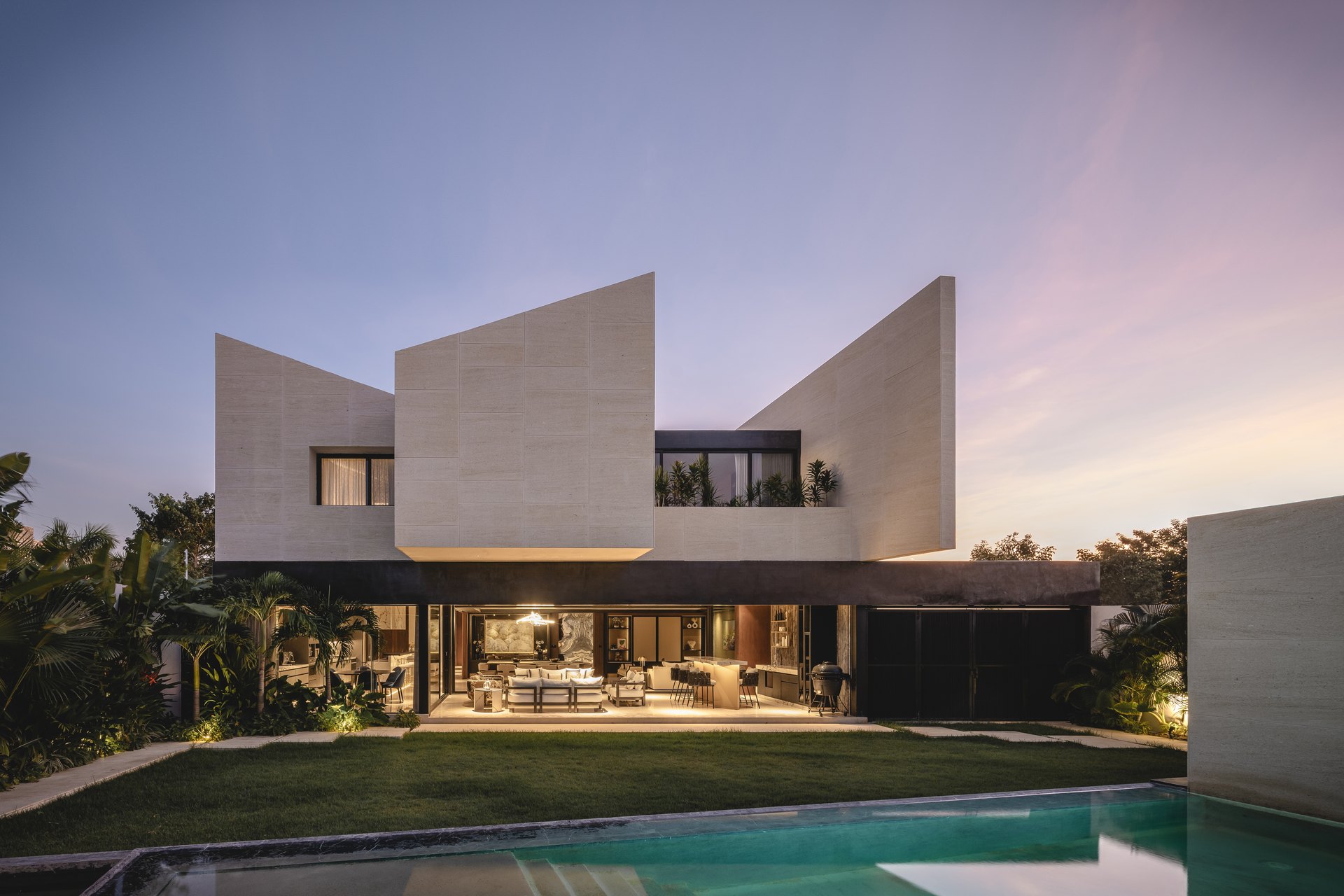 Casa Magmol, en Mérida, diseñada por Arkham Projects: los volúmenes inclinados de la fachada posterior sobre la terraza y la alberca, al atardecer