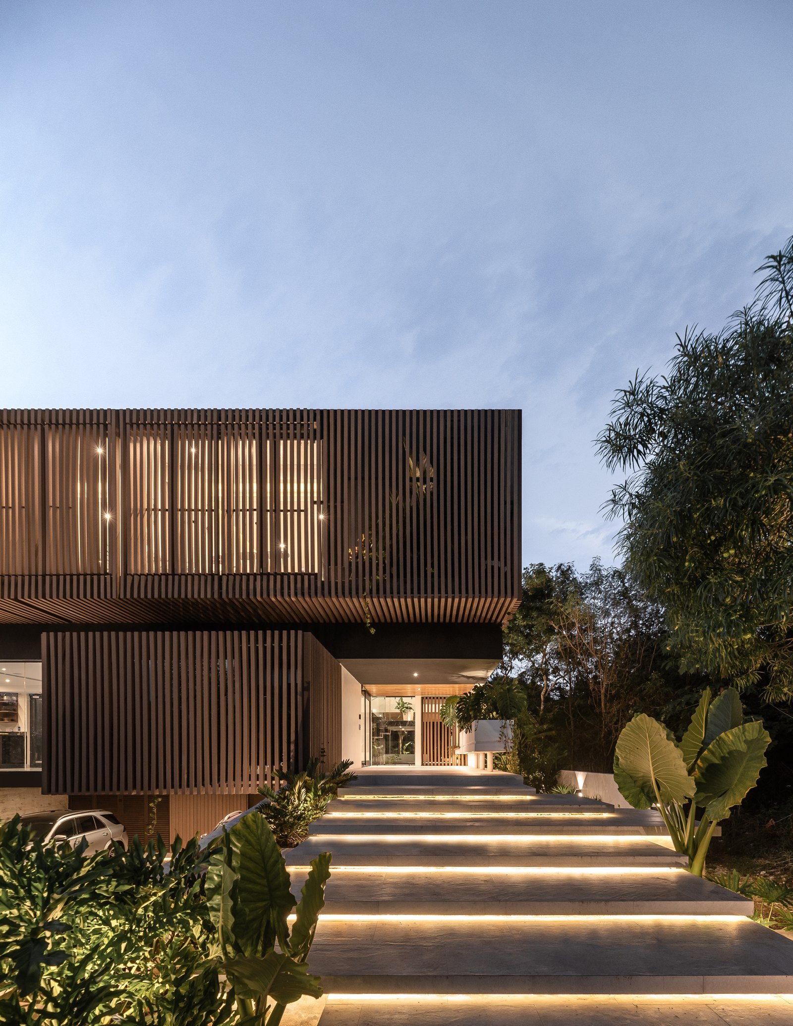 Casa Mulix de noche, diseñada por Arkham Projects: el volumen de madera iluminado desde el interior, como una gran lámpara, y la escalinata de acceso