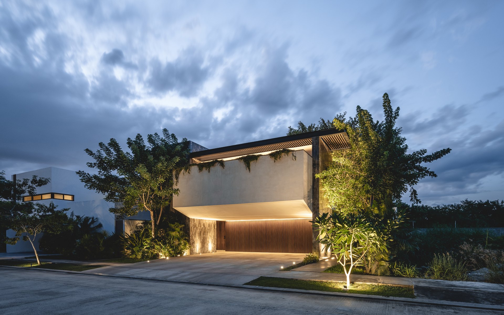 Casa Nido, en Mérida, diseñada por Arkham Projects: el volumen que vuela sobre el acceso, iluminado de noche entre los árboles
