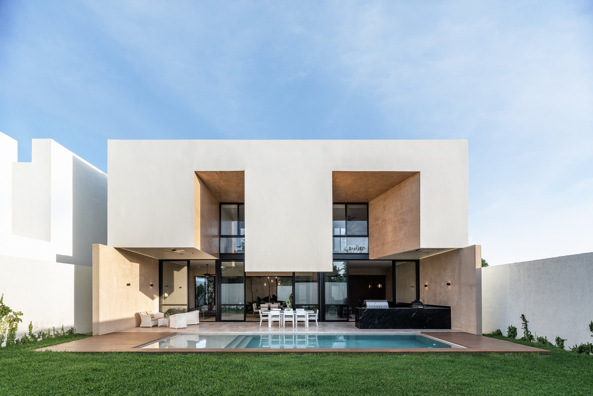 Casa Relo, en Mérida, diseñada por Arkham Projects: la fachada posterior blanca con la terraza abierta al jardín y la alberca
