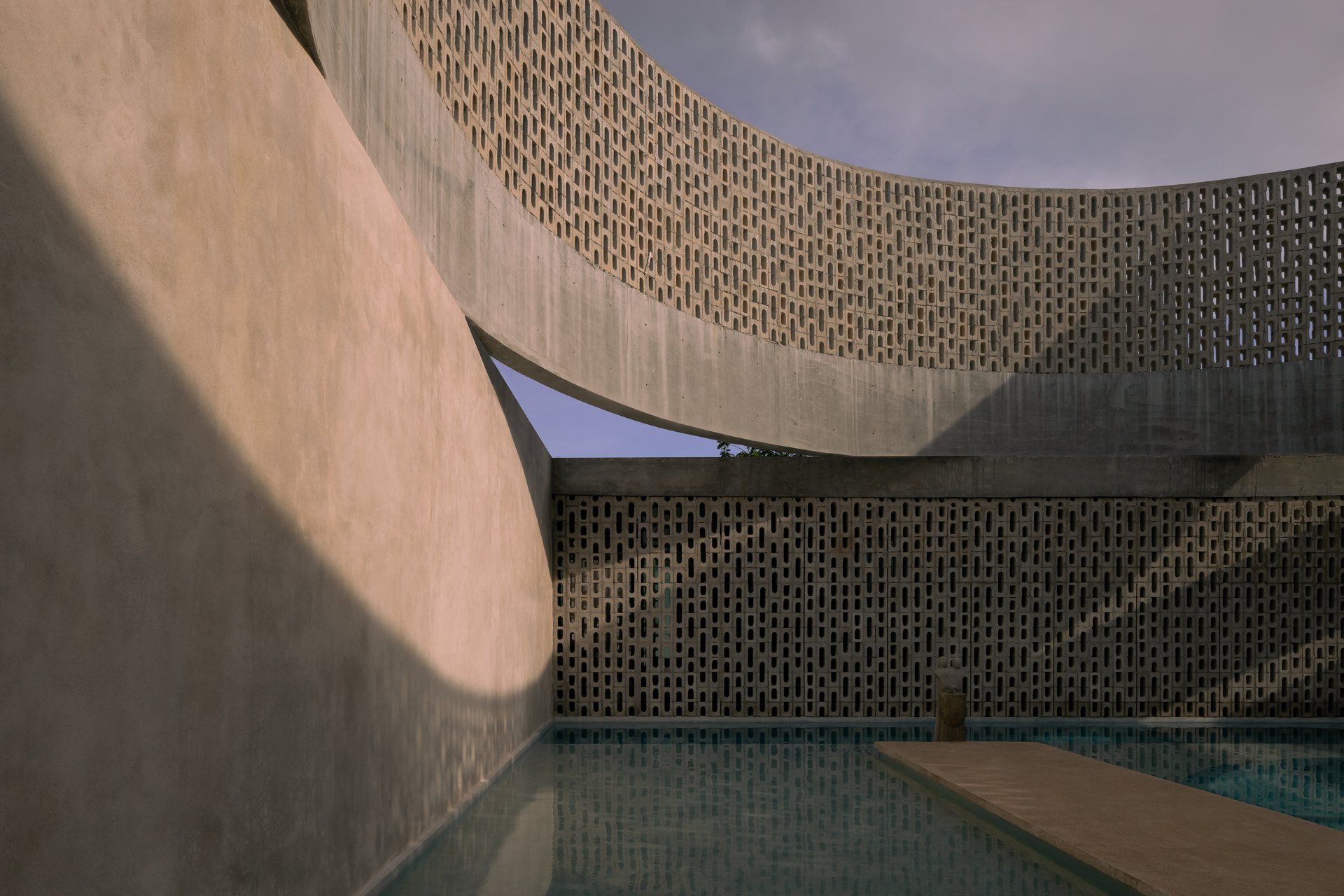 Wóolis, en Mérida, diseñada por Arkham Projects: la celosía curva de concreto sobre la alberca, con la luz del sol dibujando trazos en los muros